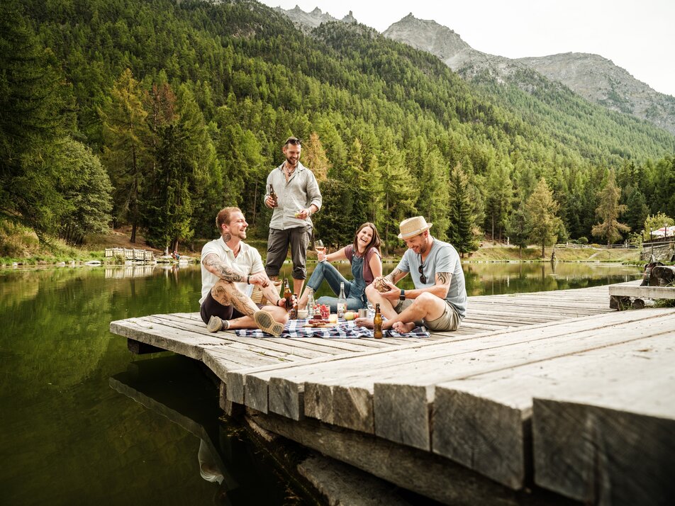 Freunde geniessen ein Picknick am See in Grächen – entspannte Sommerstimmung am Grächner See mit Wald- und Bergpanorama.